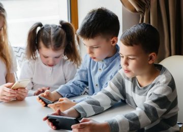 Children sit at a table in a cafe and play mobile phones together. Modern entertainment