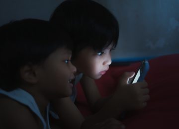 Two cute Asian boys lying on their mobile phones in a dark bedroom. Addict Playing Smartphone.Nomophobia in children.